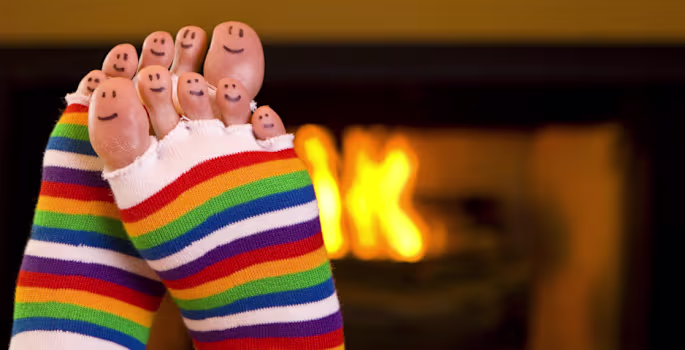 Füße in bunten Socken vor einem warm leuchtenden Kamin